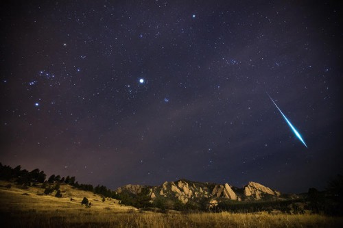 The Geminid meteor shower races over the Flatirons of Boulder, Colorado, in December 2012. A fragment burns bright enough to outshine all of the planets, producing what's called a Fireball. Orion can also be seen in the photograph trailing across the sky toward the Pleiades and the glow of Jupiter inside the constellation of Taurus.